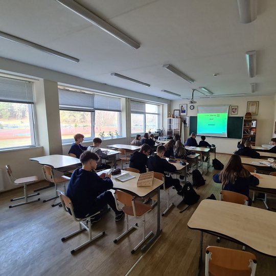 Aštuntokai sėdi klasės suoluose. Prieš juos projektoriuje matoma pamokos tema.