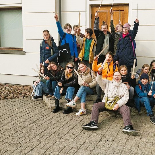 Mokiniai, karingai nusiteikę, sėdi ant Nacionalinio muziejaus įėjimo laiptų.