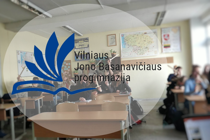 Nuotraukoje vaizduojamas Vilniaus Jono Basanavičiaus progimnazijos ženklas (logotipas), už kurio matosi mokykloje esanti klasė.