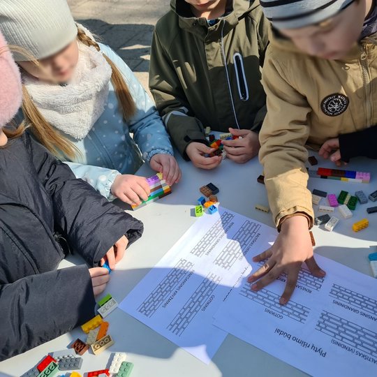Vaikai tyrinėja ant stalo padėtus lapus, kuriuose vaizduojami plytų rišimo būdai.