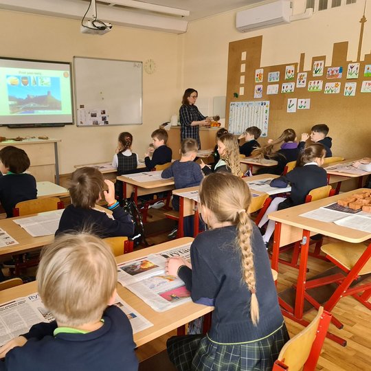 Klasėje edukatorė mokiniams demonstruoja senoviškus puodus.