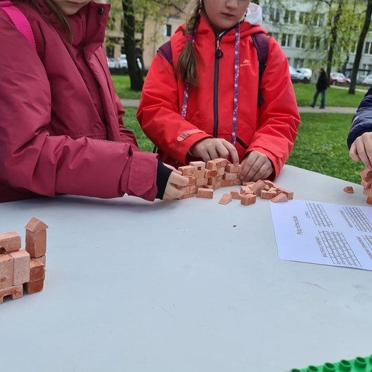 Mergaitiškos rankytės dėlioja mažas plyteles, kurios dėliojasi į pilį.