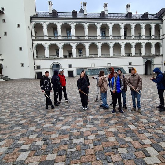 Mokinių būrelis Valdovų rūmų kieme. Jie rankose turi medinius kardelius.