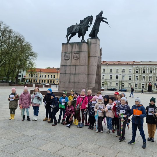 Mokiniai Katedros aikštėje, išsirikiavę į eilę. Už jų matosi Gedimino paminklas.