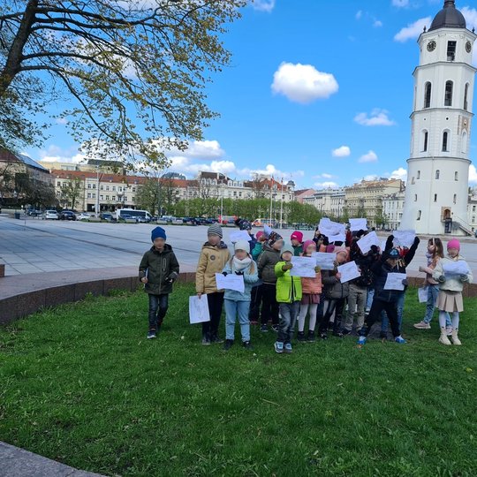 Vaikai stovi buvusio bokšto vietoje, iškėlę baltus lapus su savo kūriniais.