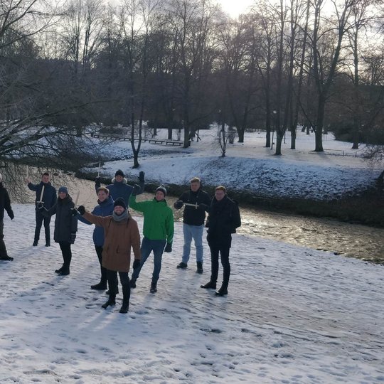 „Bitė Lietuva“ technikai, iškėlę medinius kalavijus į viršų, pozuoja nuotraukai Bekešo pliaže. Jiems už nugaros teka Vilnelė.