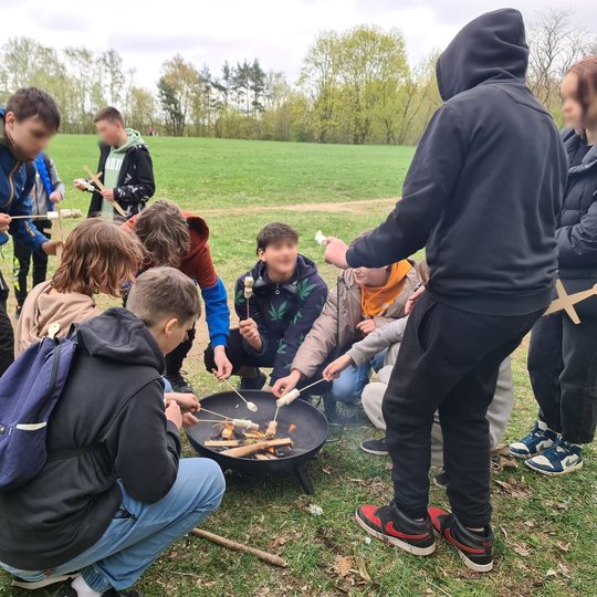 Mokiniai kepa zefyrus, susmeigtus ant pagaliukų. Juos kepa ant pačių savo užkurti laužo. 