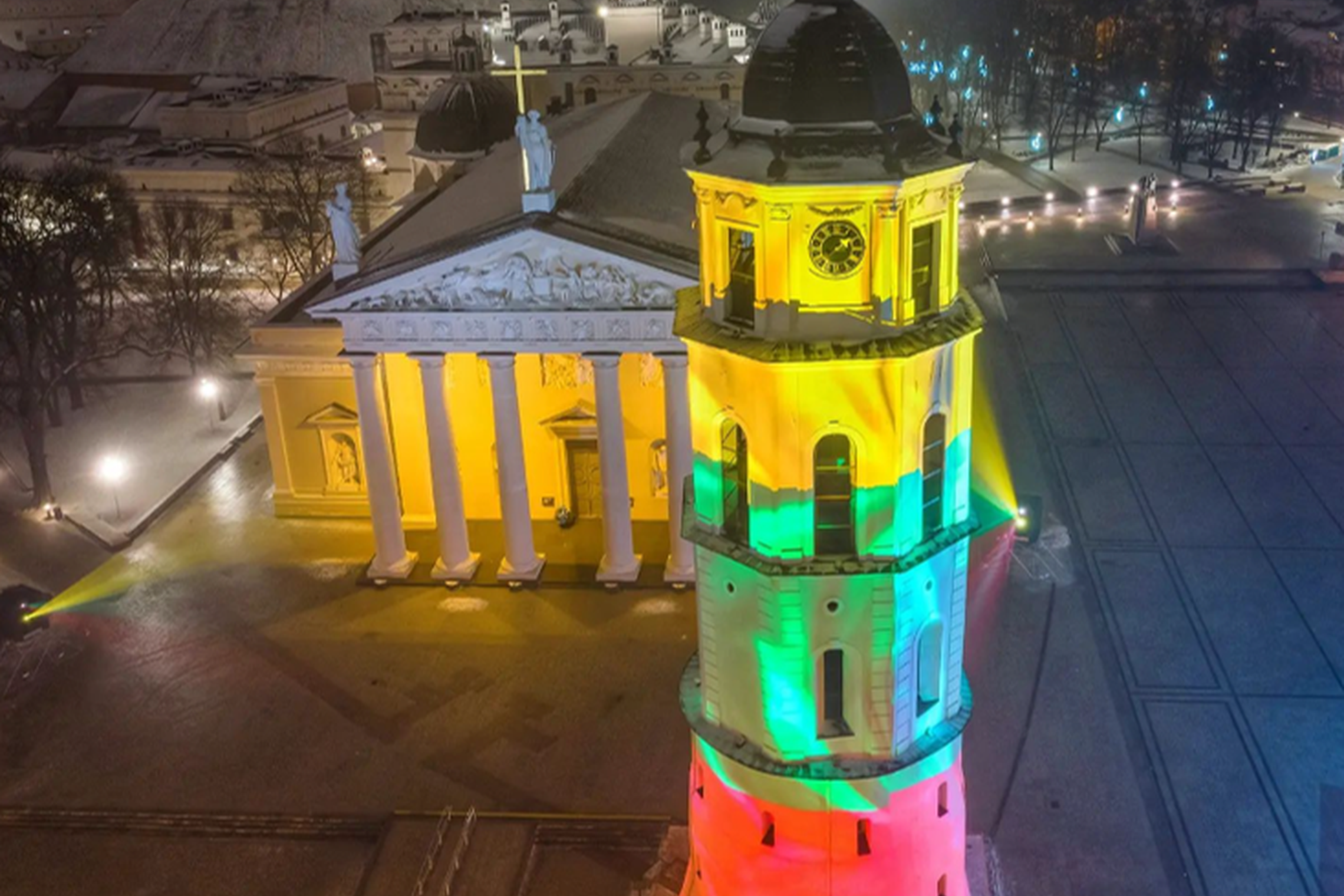 Katedra, jos varpinė ir Gedimino kalnas su pilimi nufotografuota iš oro, vakarą. Aplink daug šviesų, o katedros varpinė apšviesta trispalvės spalvomis.