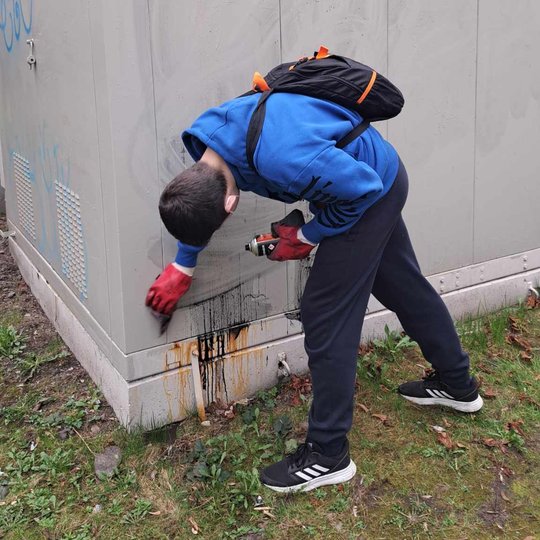 Berniukas pasilenkęs valo graffiti dažus nuo elektros transformatorinės prie Kirdiejų rūmų.
