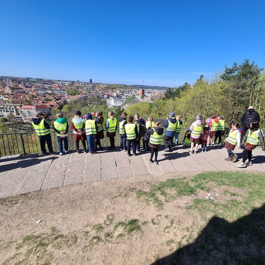 Ryškiai apsirengusių vaikų būrelis ant Trijų Kryžių kalno apžvalgos aikštelės.