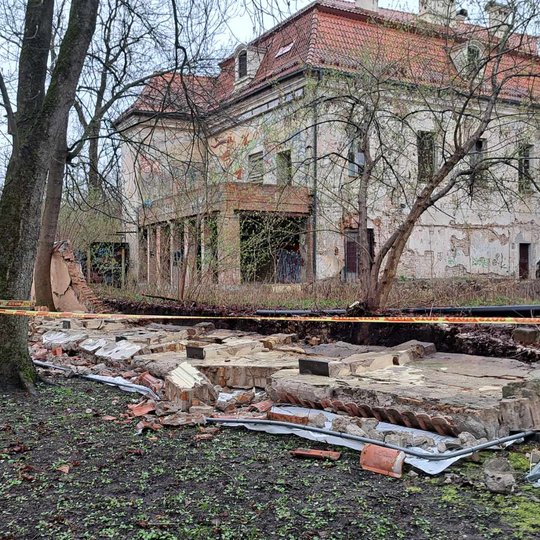 Nufotografuota nuvirtusi tvora iš arti. Tvora guli ant vejos, mėtosi plytos.