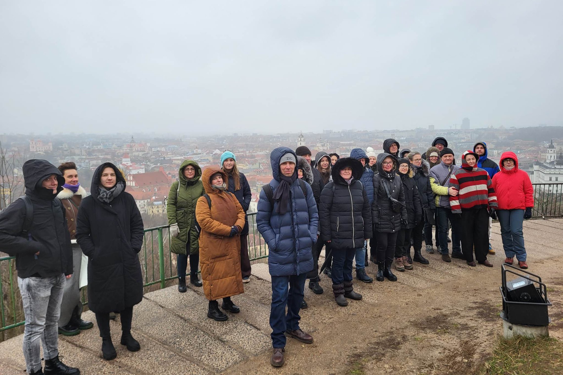Ekskursijos dalyviai pozuoja nuotraukai ant Trijų Kryžių kalvos. Jiems už nugaros matosi Vilniaus senamiesčio panorama.  