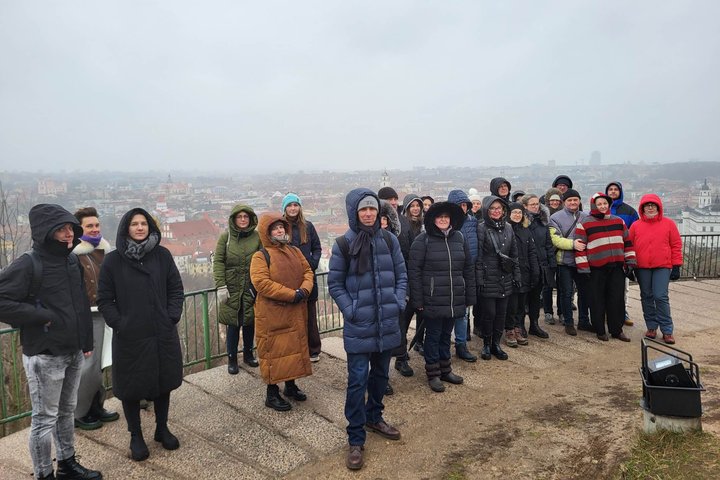 Ekskursijos dalyviai pozuoja nuotraukai ant Trijų Kryžių kalvos. Jiems už nugaros matosi Vilniaus senamiesčio panorama.