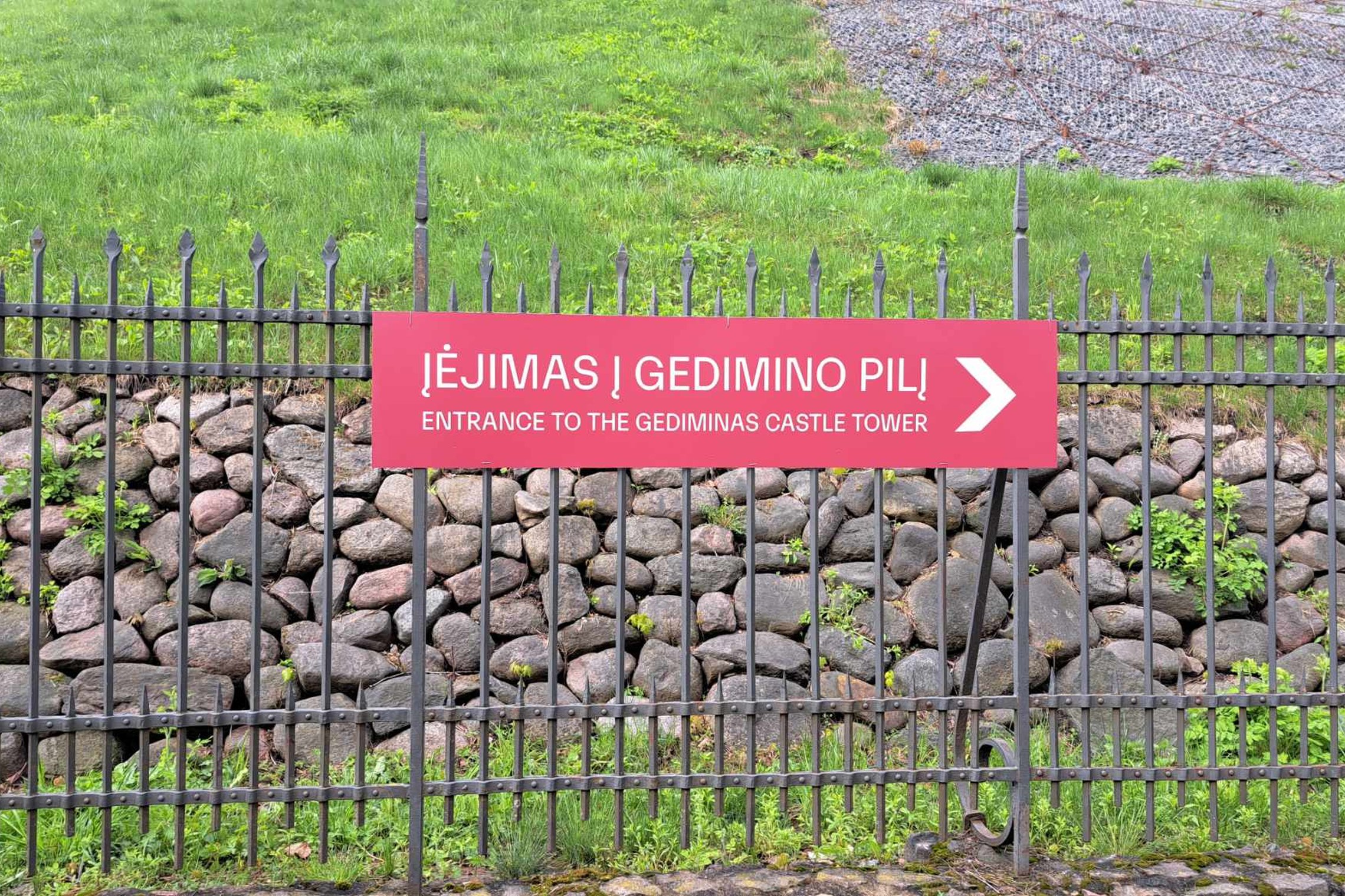 Raudona informacinė lentelė, nurodanti kryptį į Gedimino pilies kalną. Ši rodyklė yra pietinėje kalno papėdėje. Nuotraukoje ji atnaujinta, švari.