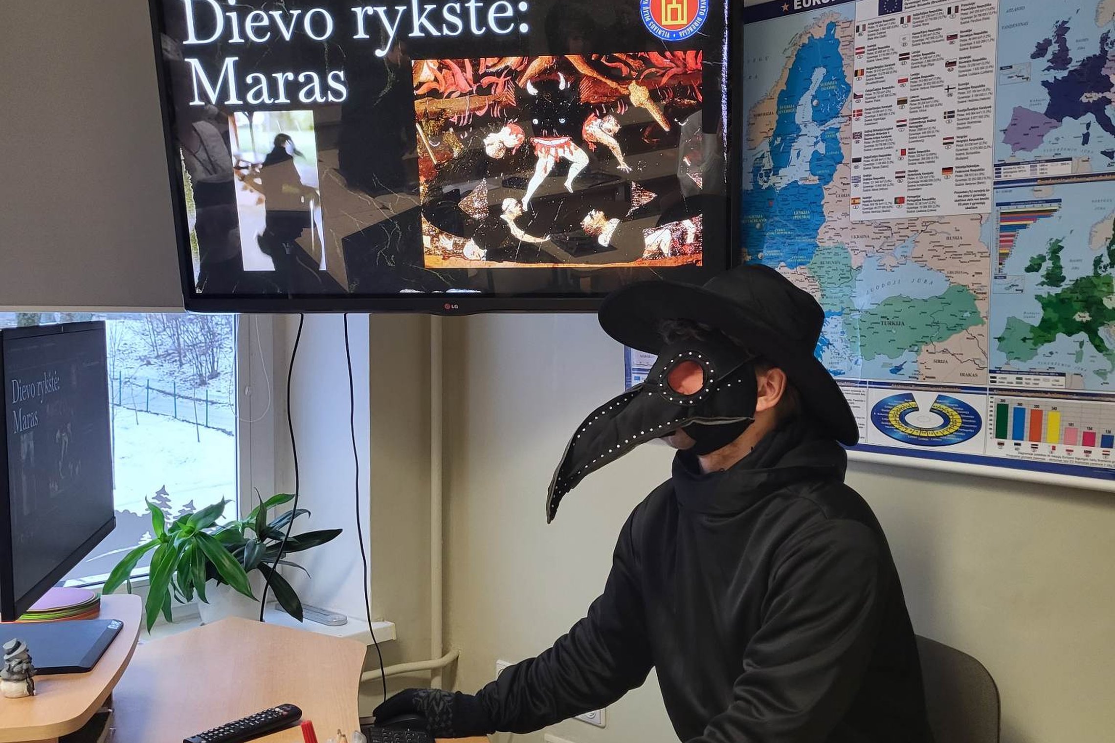 Edukatorius, apsivilkęs juodą maro daktaro kostiumą, sėdi prie kompiuterio ir veda pamoką apie marą aštuntokams.