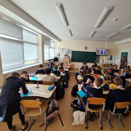 Nufotografuota mokinių klasė iš pačio klasės galo. Klasės priekyje matoma ir klasės vadovė.