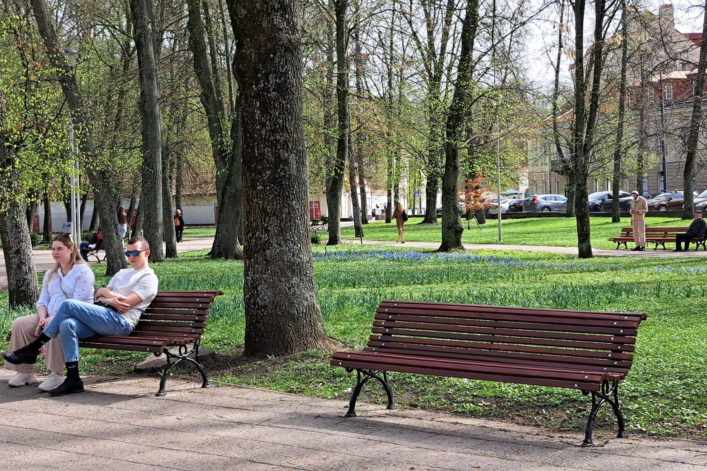 Sereikiškių parke nufotografuoti žmonės, sėdintys ant dviejų atrestauruotų lauko suolų.