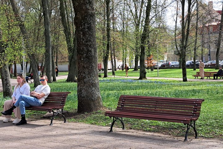 Sereikiškių parke nufotografuoti žmonės, sėdintys ant dviejų atrestauruotų lauko suolų.