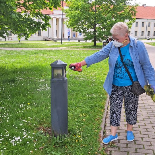 Savanorė purškia valikliu išpieštą šviestuvą Mindaugo skvere.