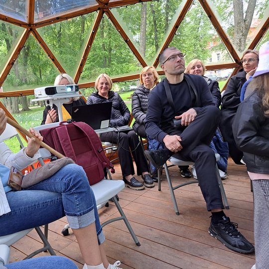 Paskaitos klausytojai apžiūri medinius įrankius rankose.