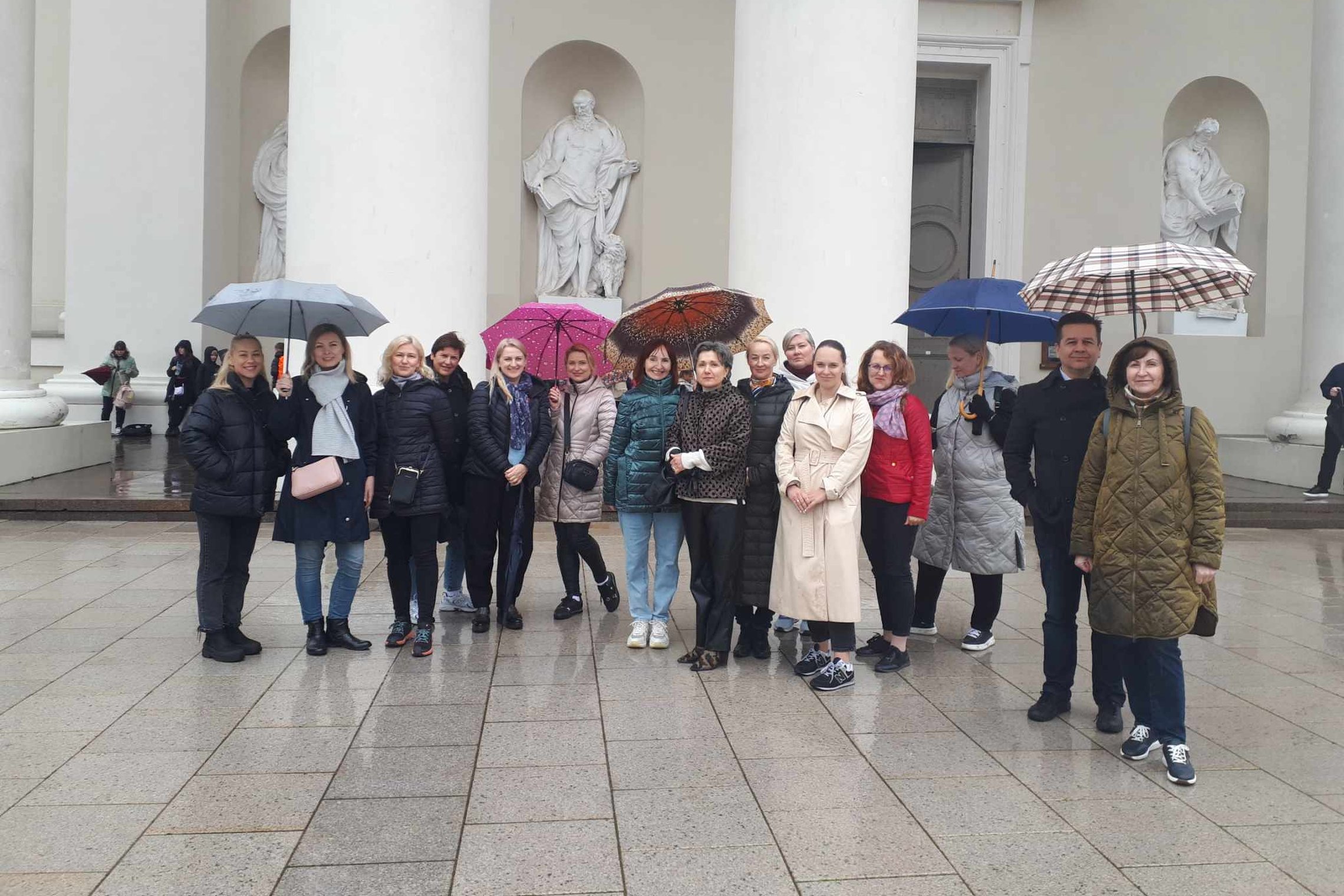 Ekskursantai Katedros aikštėje, prie Katedros fasado. Kai kurie laiko skėčius.
