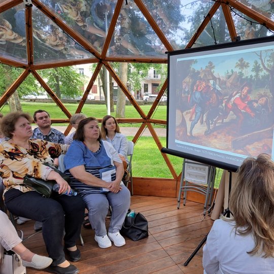 Grupė žmonių sėdi Vilniaus pilių kupole ir žiūri į paskaitos prezentaciją.