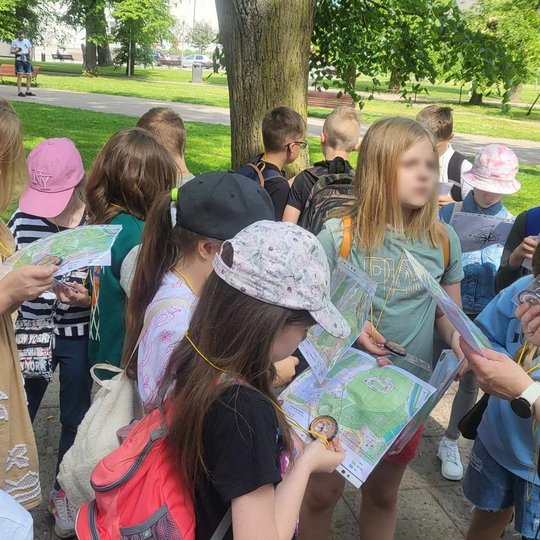 Grupė mokinių ir edukatorė rankose laiko Vilniaus pilių planus.