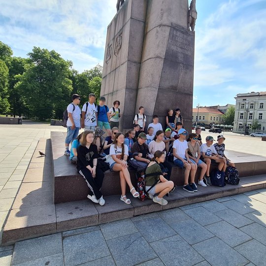 Mokinių grupė pavėsyje, prie Gedimino paminklo Katedros aikštėje.