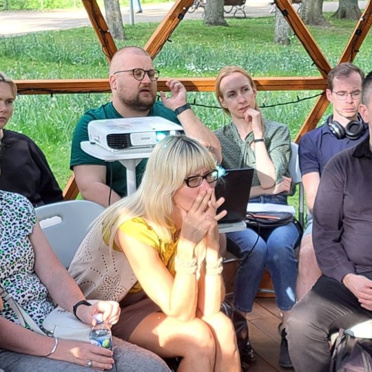 Grupė žmonių sėdi Vilniaus pilių kupole ir žiūri į paskaitos prezentaciją.