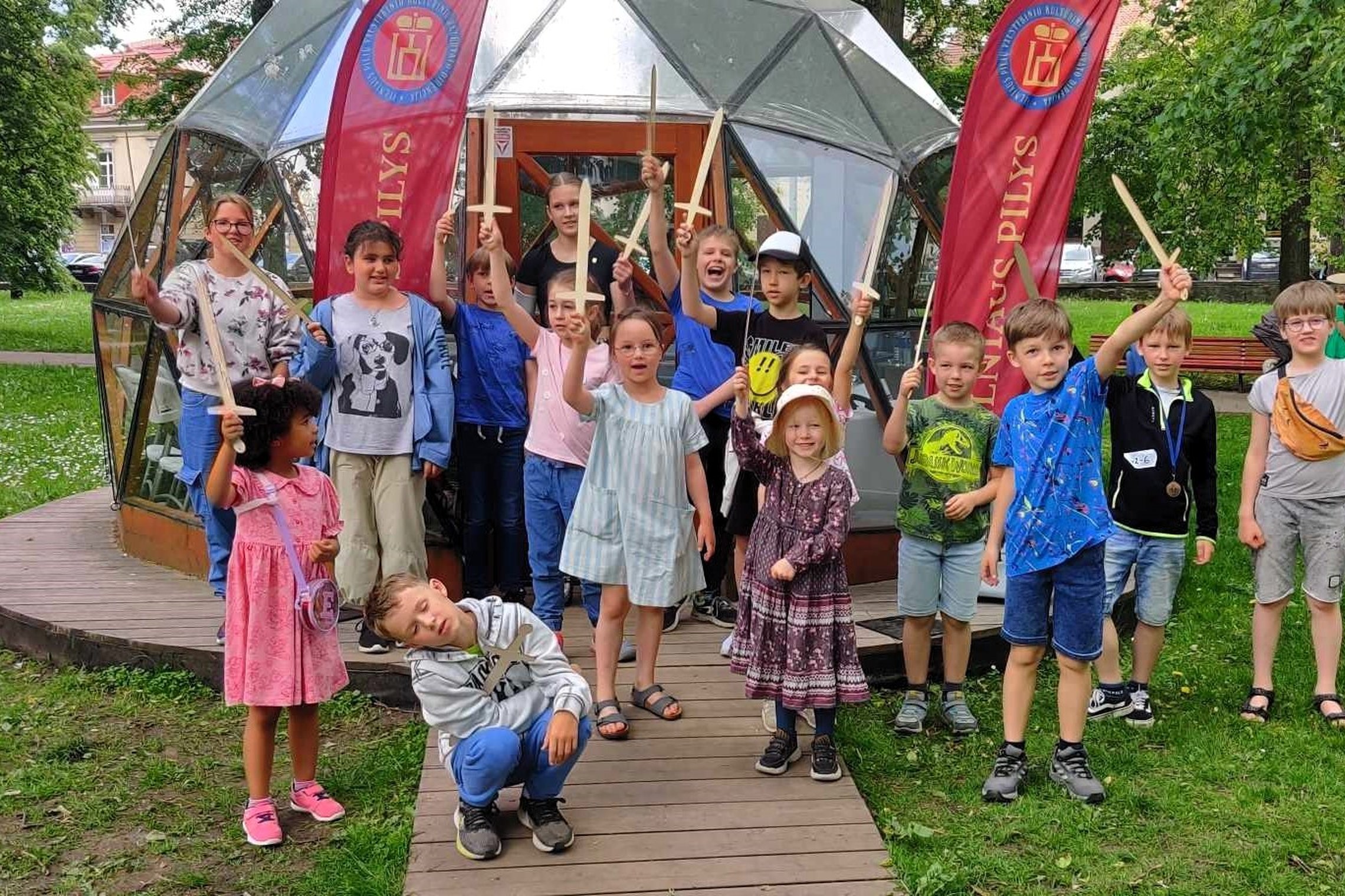 Vaikai stovi prie Vilniaus pilių kupolo iškėlę į viršų medinius kardus.