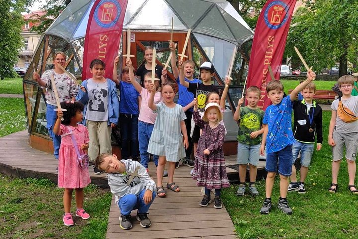 Vaikai stovi prie Vilniaus pilių kupolo iškėlę į viršų medinius kardus.