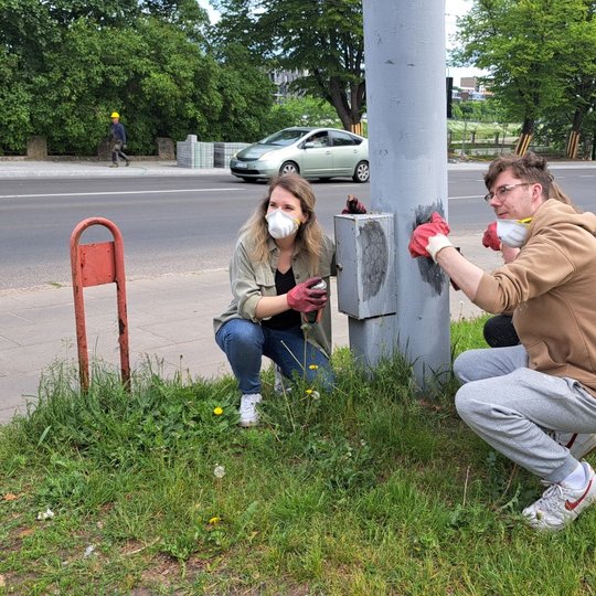 Du savanoriai pozuoja, valydami elektros stulpą prie Kalnų parko.