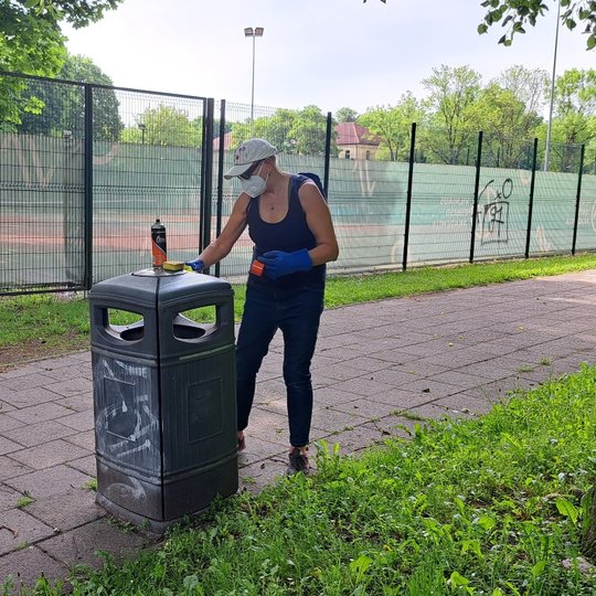 Viena savanorė valo šiukšliadėžę prie teniso kortų.