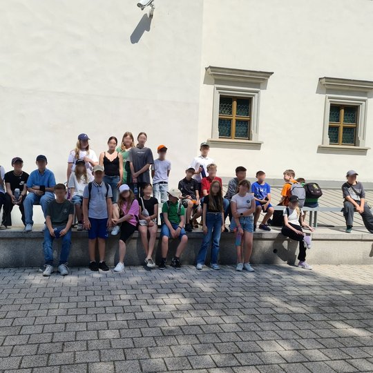 Mokinių grupė ant granito plokštės prie Valdovų rūmų sienos.