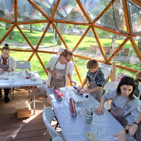 Moterys ir vienas vaikas Vilniaus pilių kupole minko molį. Jie dėvi prijuostes.