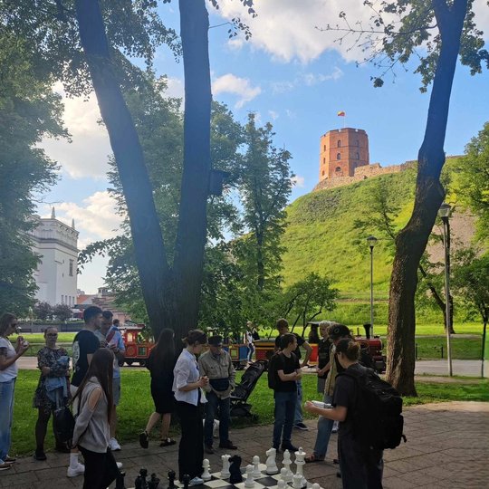 Žmonės žaidžia gigantiškais, ant žemės sudėliotais šachmatais.