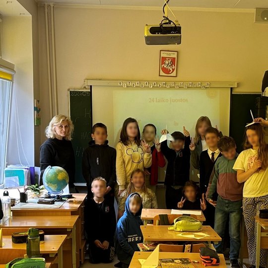 Mokiniai ir mokytoja išsirikiavę klasės priekyje bendrai nuotraukai.