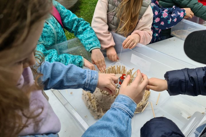Vaikučiai lipdo smėlio pilį ir smeigia į ją medinius pagaliukus.