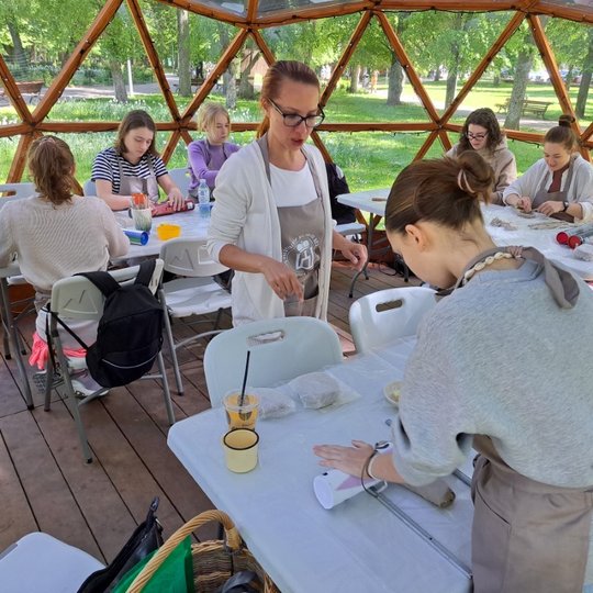 Molininkė pasakoja instrukcijas merginai, kaip reikia lipdyti, o ji bando pagaminti molinį gaminį.