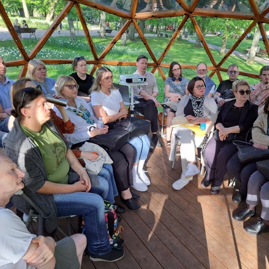 Paskaitos klausytojai sėdi kupole ir žiūri į projektorių.