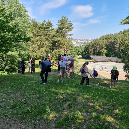 Grupė bėgiojančių vaikų Kalnų parke. Už jų matosi estrada.