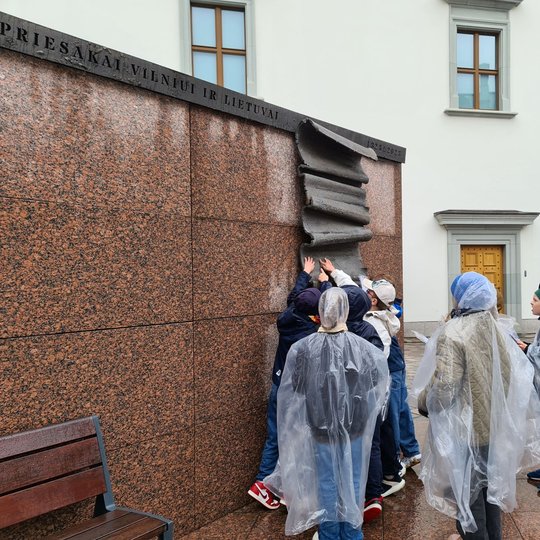 Vaikai su lietpalčiais Valdovų rūmų kieme, prie Gedimino laiško paminklo.