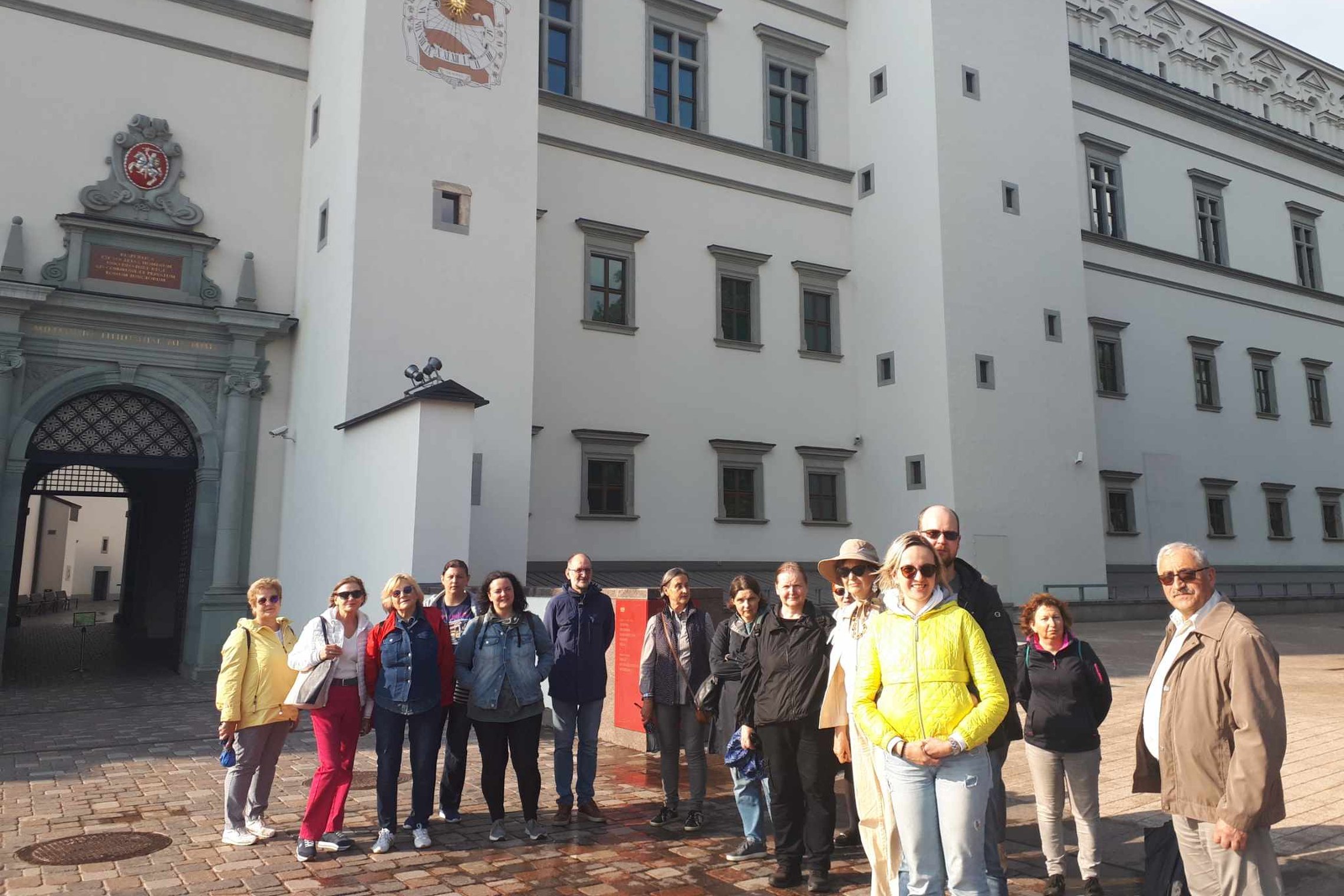 Ekskursijos grupė stovi prie Valdovų rūmų, Katedros aikštėje.