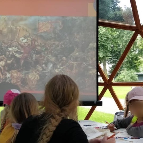 Vaikai žiūri į Žalgirio mūšio paveikslą projektoriaus  ekrane.