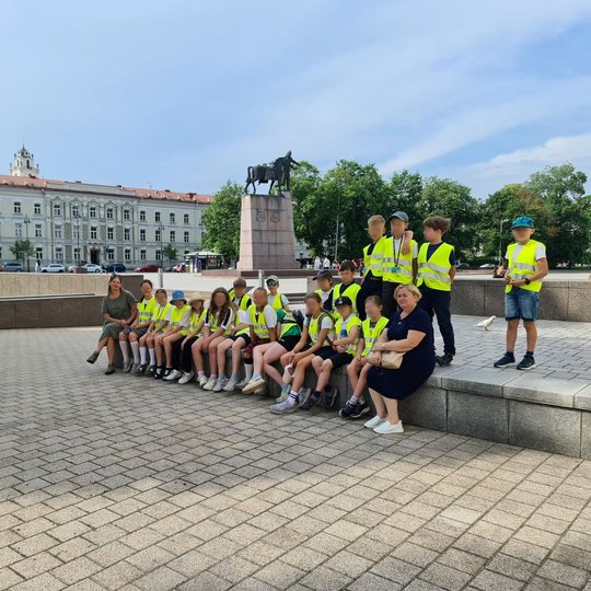 Mokinių grupė susėdę Katedros aikštės pavėsyje.