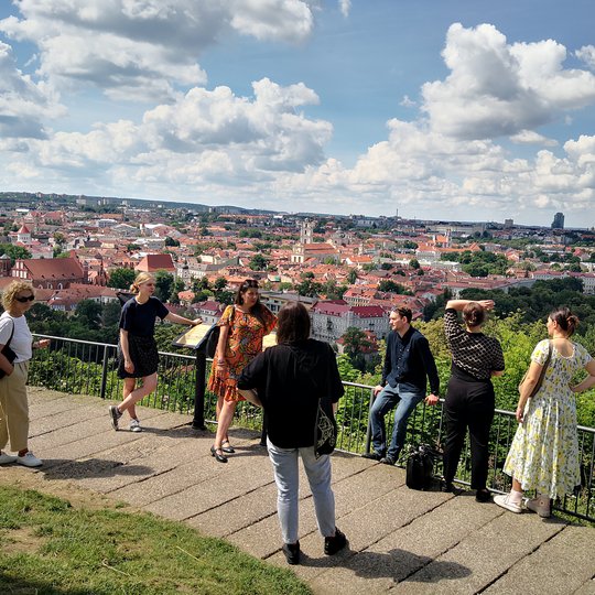 Ekskursijos dalyviai ir gidė ant Trijų Kryžių kalno apžvalgos aikštelės. Už jų matosi Vilniaus senamiesčio panorama.