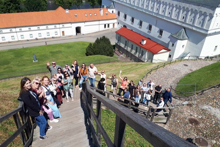 Didelė grupė ekskursijos dalyvių mojuoja kamerai nuo Gedimino pilies kalno laiptų.