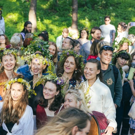 Plačiai besišypsančių moterų su vainikais ant galvų šypsosi bendrai nuotraukai.