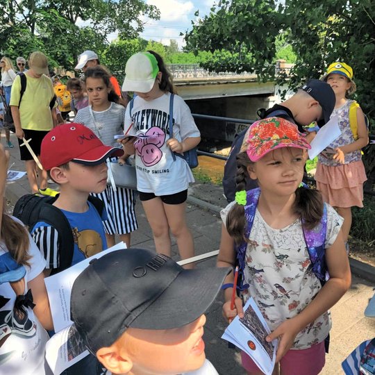 Mokiniai prie Vilnios upės rankose laiko užduočių lapus orientacinei edukacijai.