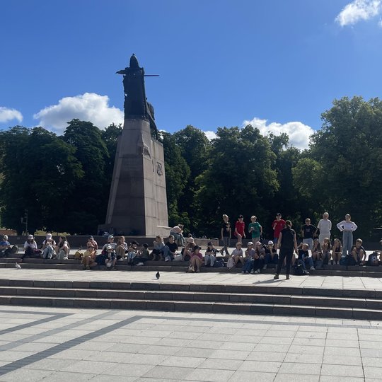 Vaikų gausi eilė sėdi Katedros aikštėje ant laiptų, prie Gedimino paminklo.
